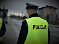 policjant mikołowskiej drogówki, w kamizelce odblaskowej stoi na drodze. Ma założoną maseczkę. Stoi tyłem do fotografa