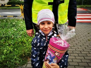 mała dziewczyna stoi przed policjantem i trzyma w ręce papierową torbę ze słodyczami