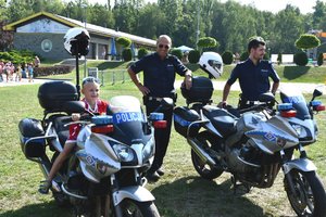 dziecko siedzące na policyjnym motocyklu, obok stoją dwaj policjanci