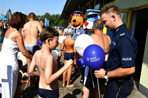 policjant rozdaje dzieciom balony, w tle maskotki śląskiej i mikołowskiej policji