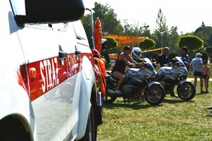 samochód straży pożarnej, a w tle kobieta siedząca na policyjnym motocyklu