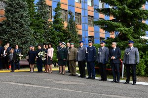 Zdjęcie kolorowe. Widoczni umundurowani policjanci oraz osoby cywilne biorący udział w uroczystości przed budynkiem komendy wojewódzkiej policji