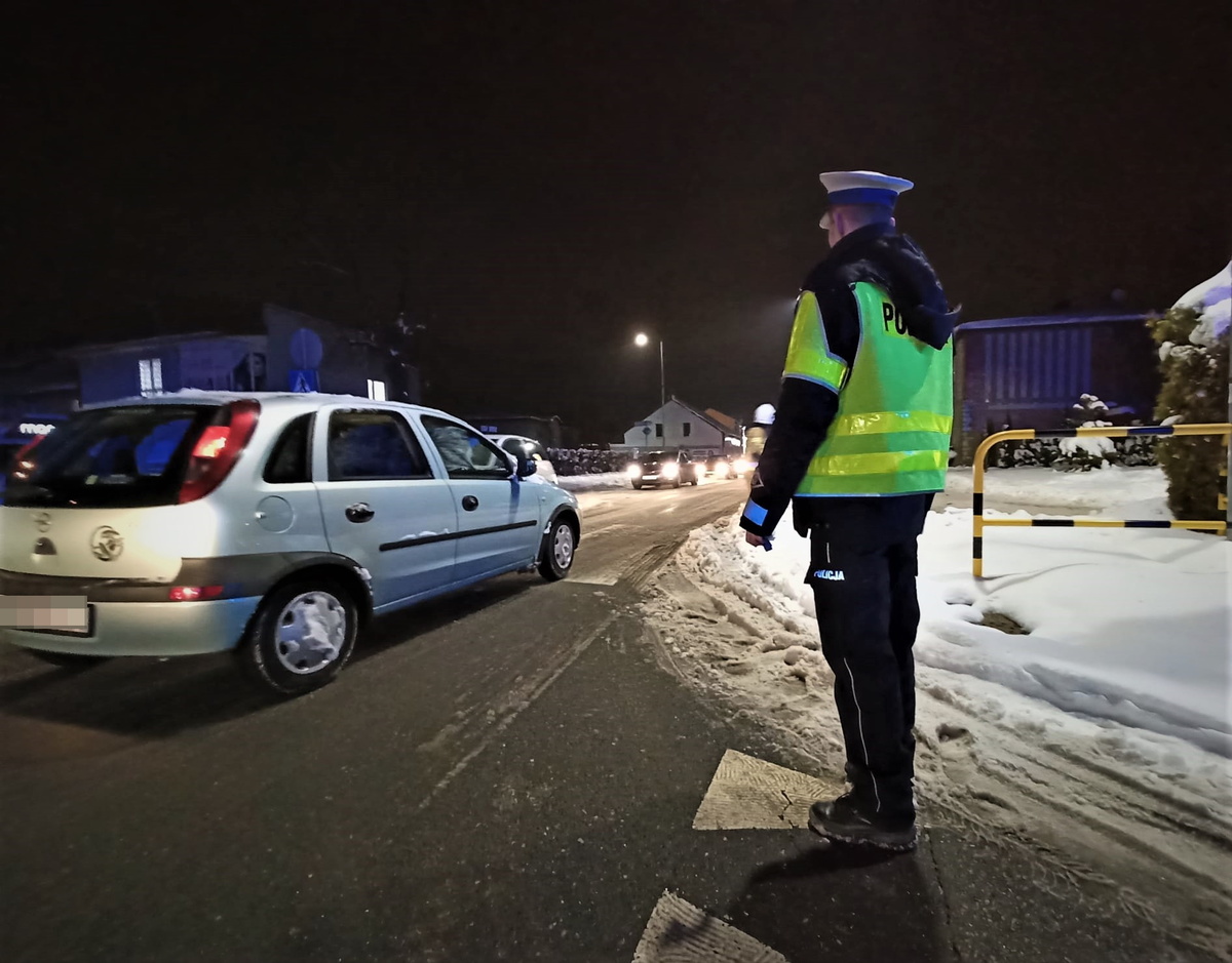 na zdjęciu widać policjanta drogówki w odblaskowej kamizelce, obok niego samochód osobowy, jest pora wieczorna