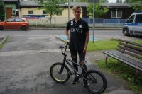 zdjęcie przedstawia 15 letniego Piotrka z odzyskanym przez policjantów rowerem bmx, w tle widać budynek i radiowóz