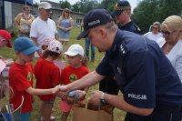 na zdjęciu na pierwszym planie widać policjanta gratulującego i wręczającego prezent za uczestnictwo w spartakiadzie przedszkolakowi