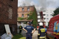 na zdjęciu na pierwszym planie policjant ze strażakiem, w tle płonąca kamienica