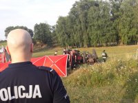 na zdjęciu widać na pierwszym planie policjanta, a w tle przewrócony w polu ciągnik rolniczy