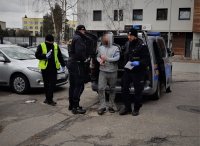 na zdjęciu: policjanci prowadzą zatrzymanego mężczyznę, parking komisariatu