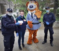 na zdjęciu: policjanci z Komisariatu Policji w Łaziskach Górnych pozują z maskotką oraz jedną z mieszkanek miasta. Akcja rozdawania maseczek.