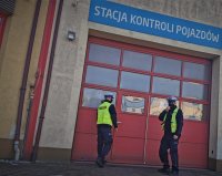 dwoje umundurowannych policjantów stoi przed wejściem do budynku stacji kontroli pojazdów w Łaziskach Górnych