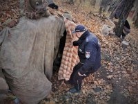 na zdjęciu widać umundurowanego policjanta, który podnosi kotarę zasłaniającą wejście do bunkra zajmowanego przez bezdomnych. Las w Łaziskach Górnych