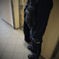 fragment nóg zatrzymanego oraz policjanta przy kracie pomieszczenia dla zatrzymanych