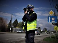 umundurowany policjant drogówki kontroluje prędkość na jednej z dróg, trzyma w ręce fotoradar. Usta i noc ma zasłonięte maseczką
