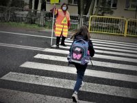 mała dziewczynka, uczennica szkoły, przechodzi przez oznakowane przejście dla pieszych