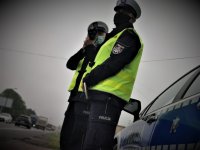 dwóch policjantów w odblaskowych kamizelkach stoi przy drodze i kontroluje prędkość