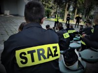 napis STRAŻ na zewnętrznej części odzieży, w tle widać policjanta, który prowadzi szkolenie