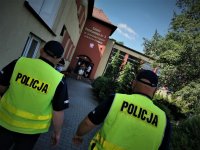 umundurowani policjanci w odblaskowych kamizelkach wchodzą na teren szkoły