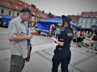 policjantka rozdaje ulotki informacyjne. Scena ma miejsce na płycie rynku