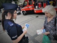 policjantka rozdaje ulotki informacyjne. Scena ma miejsce na płycie rynku