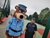 policjant z maskotką przechadza się po terenie boiska szkolnego i placu zabaw dla dzieci