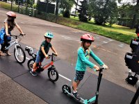 dzieci jadące na hulajnogach oraz rowerze