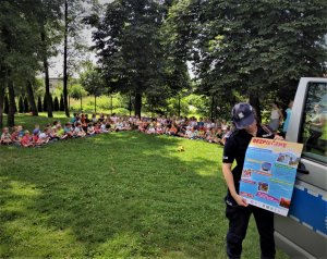 policjantka prezentuje plakat dotyczący bezpiecznych wakacji, w tle grupa dzieci