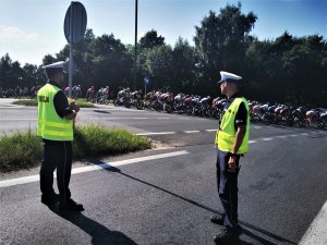 stojący przy trasie wyścigu kolarskiego policjanci, w tle peleton