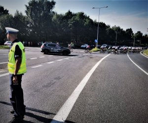 stojący na trasie policjant, w tle samochód reklamowy Tour de Pologne