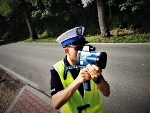 policjant drogówki trzyma w ręce miernik prędkości i dokonuje pomiaru