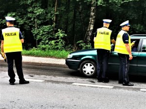 trzech policjantów drogówki, ubranych w odblaskowe kamizelki, stoi na drodze i kontroluje trzeźwość kierowców