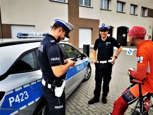 policjanci drogówki w trakcie kontroli rowerzysty, w tle budynek, obok nich mężczyzna w pomarańczowym ubraniu