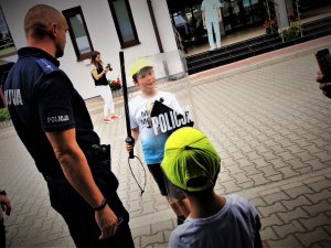 policjant prewencji rozmawia z małymi dziećmi, pokazuje im służbowy sprzęt
