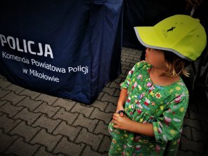mała dziewczynka w zielonej sukience i odblaskowej czapce, w tle logo &quot;Komenda Powiatowa Policji w Mikołowie&quot;