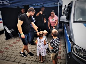 policjant rozmawia z rodzicami i ich dziećmi, w tle stoisko mikołowskiej Policji