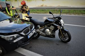 przednia część osobówki marki bmw oraz motcykl, w tle policjant i strażak