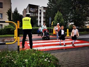 policjant drogówki pomaga dzieciom i ich rodzicom w bezpiecznym przejściu przez pasy