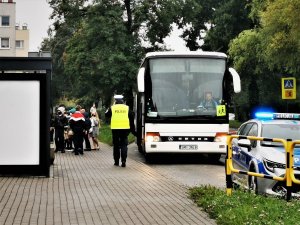 policjant drogówki podchodzi do szkolnego autobusu, widać także oznakowany radiowóz