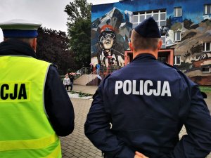 policjant drogówki i dzielnicowy zwróceni twarzą w kierunku budynku szkoły podstawowej