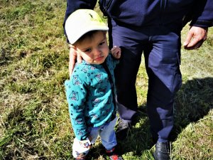 3-letni chłopiec z założoną czapeczką z logo kampanii, za nim stoi policjant