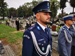 policjant lektor z Komendy Wojewódzkiej Policji, obok niego stoją policjanci z policyjnej orkiestry