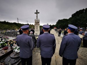 trzech umundurowanych policjantów stoi tyłem, w tle pomnik pamięci policjantów II RP