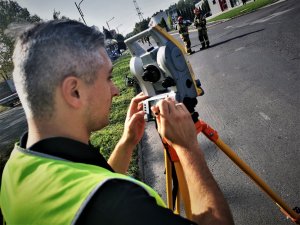 policjant drogówki w odblaskowej kamizelce pracuje na drodze, obsługuje tachimetr