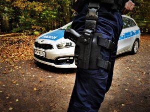 zdjęcia policjanta pionu prewencji, zbliżenie na kaburę, w tle radiowóz