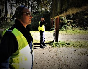 stojący obok siebie policjanci drogówki. Mają założone ochronne nauszniki