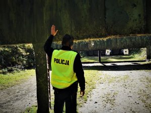 policjant w odblaskowej kamizelce stoi przed tarczą i ma podniesioną lewą rękę