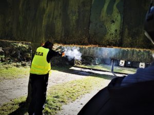 oddający strzał do tarczy policjant, za nim stoi instruktor