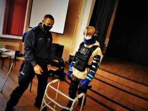 policjant pomaga uczniowi przejść kawałek drogi z tak zwanym balkonikiem