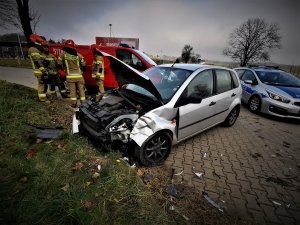 rozbity samochód koloru srebrnego, z tyłu strażacy