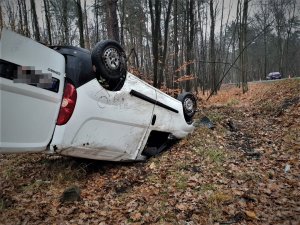 samochód koloru białego leży w rowe, wywrócony podwoziem do góry