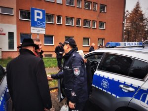 Komednant Powiatowy Policji w Mikołowie rozmawia z samorządowcami, obaj stoją przy oznakowanych radiowozach, w tle budynek komendy